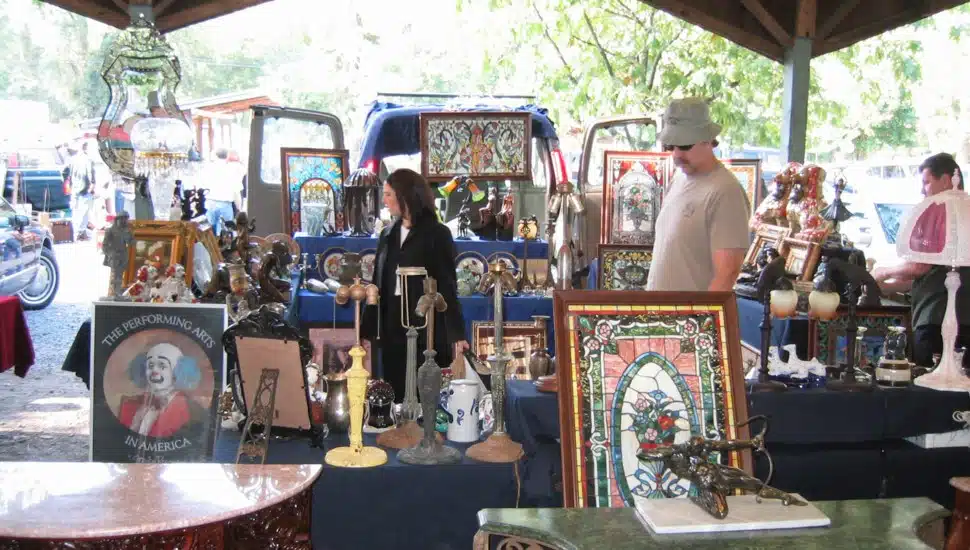 Three people walking between tables of antiques at the Golden Nugget Flea Market.