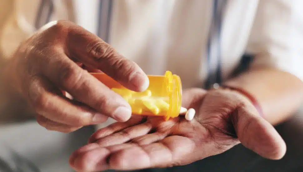 Hands, pills and bottle in closeup for man with prescriptions.