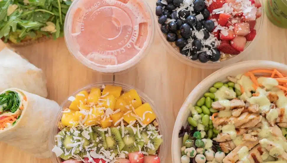 A smoothie, smoothie bowls, a wrap, and a salad on a table.