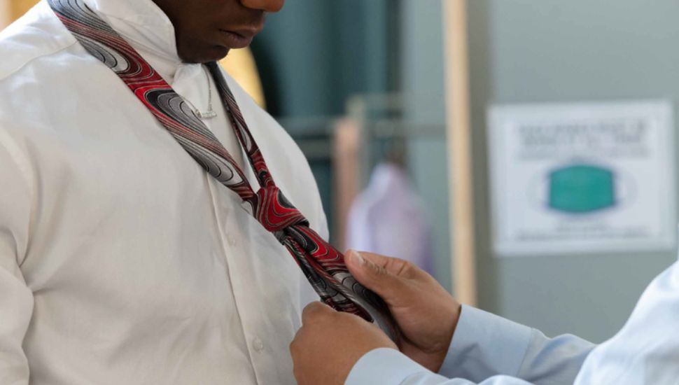 Man helping a man in a dress shirt put on a tie in The Wardrobe.
