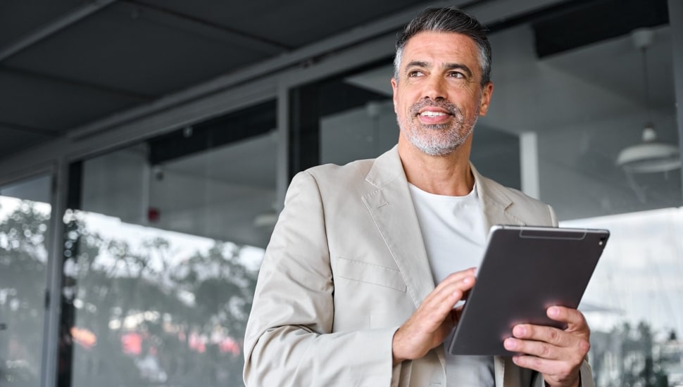 Smiling middle-aged businessman standing outside office holding digital tablet.
