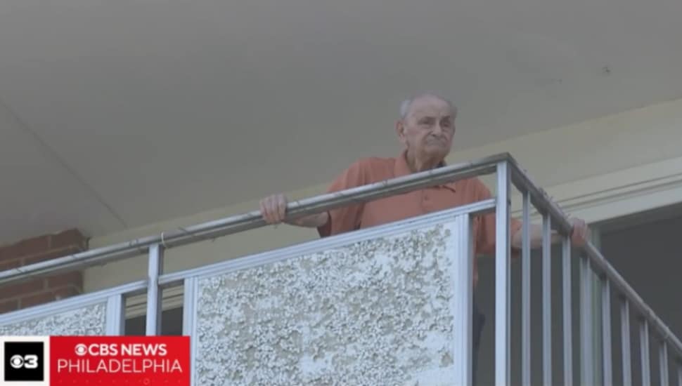 Elderly man looking out over his apartment's balcony.