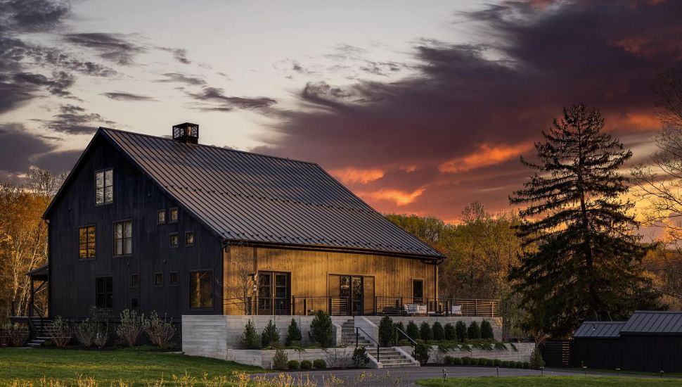 Exterior of large converted barn with dark paneling at sunset.
