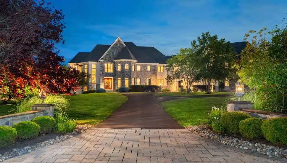 Mediterranean mansion with stone exterior and a road leading up to it surrounded by a few trees.