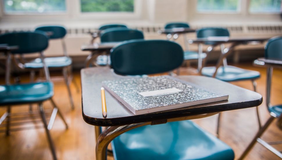 A notebook and pencil on a desk in a school classroom.