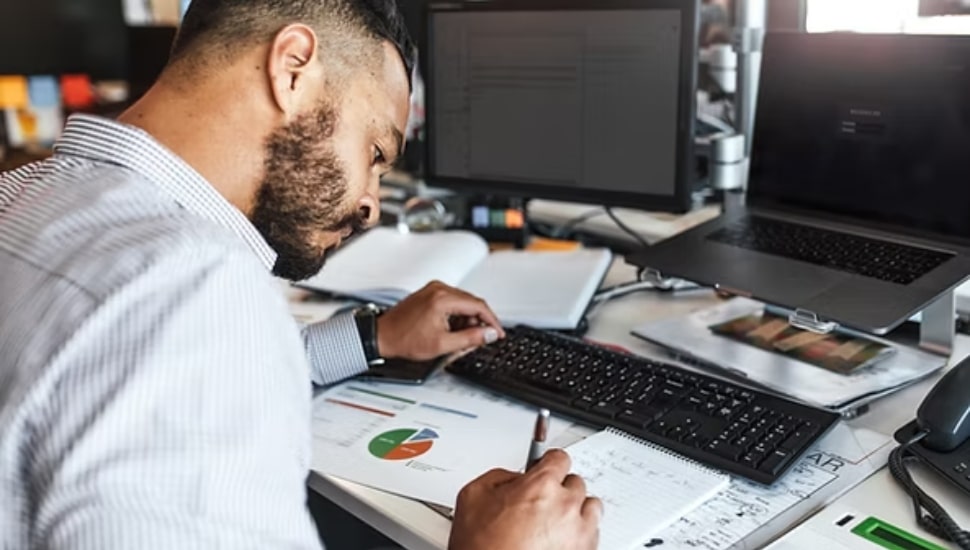 Man working at desk and writing on a notepad.