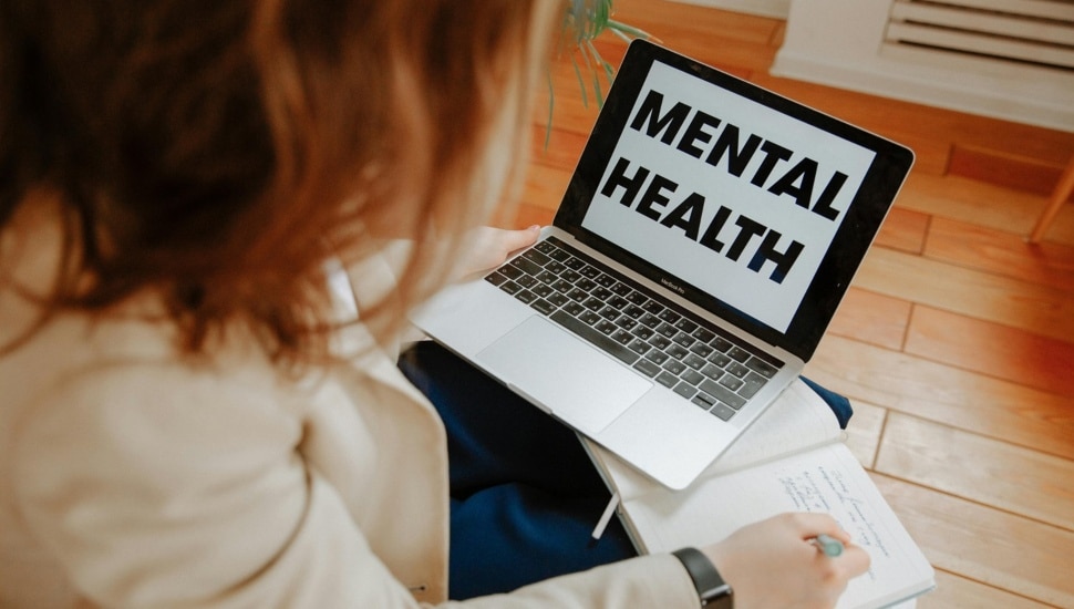 Woman looks at laptop computer with the words Mental Health on screen.