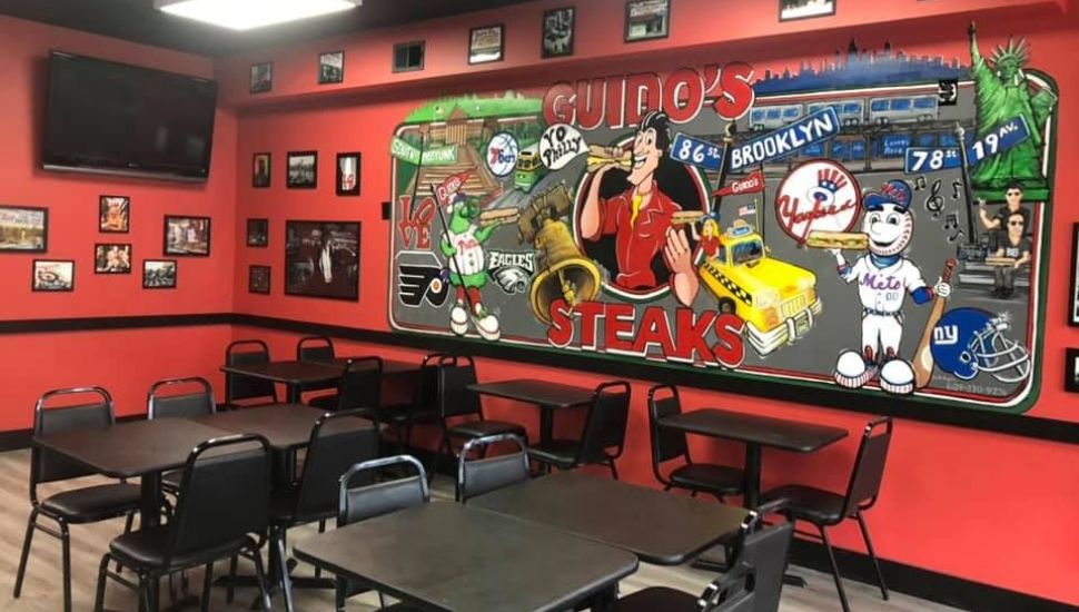 Interior of Guido’s Steaks & Pizza with tables and sign on wall.