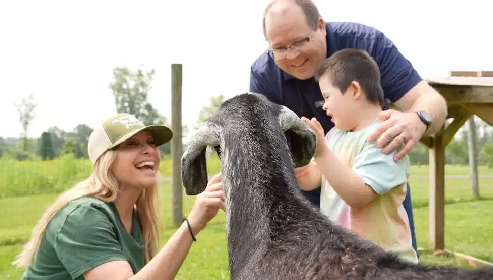 Jessica Zander with two visitors petting a goat at Helping Friendly Farm.