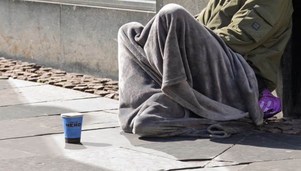 A homeless man sits on a street corner.