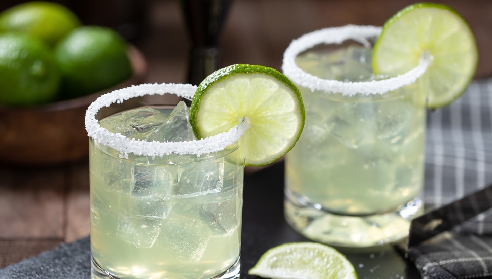Two margaritas in clear glasses with lime slices and a salted rim.