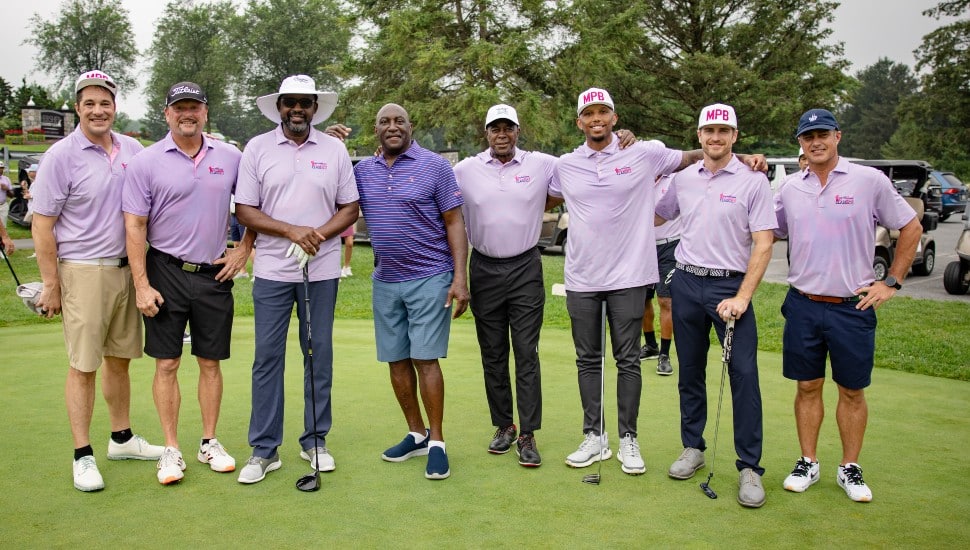 Former football players pose for a group photo on a golf green.