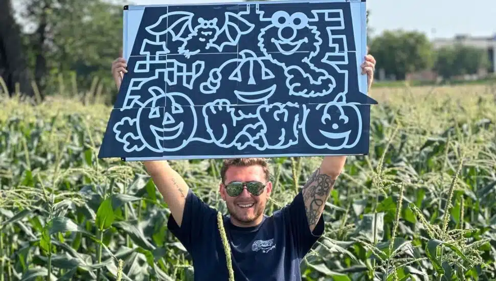 Man holding up poster with the Sesame Street corn maze design at Shady Brook Farm.