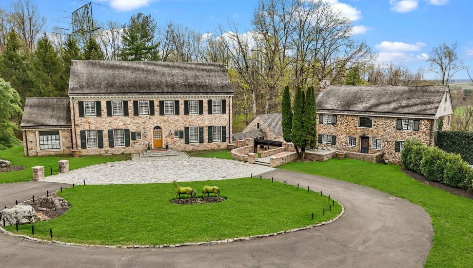 Large stone manor with a well-manicured lawn and driveway.