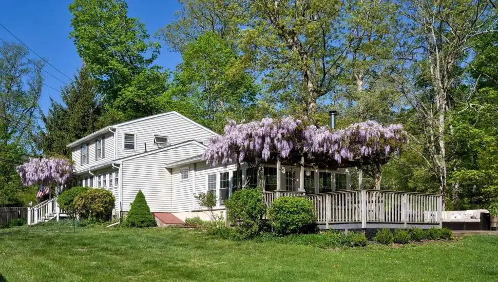 Two-story home with white siding and a back deck with a trellis covered in purple flowers at 7411 Tohickon Hill Road.