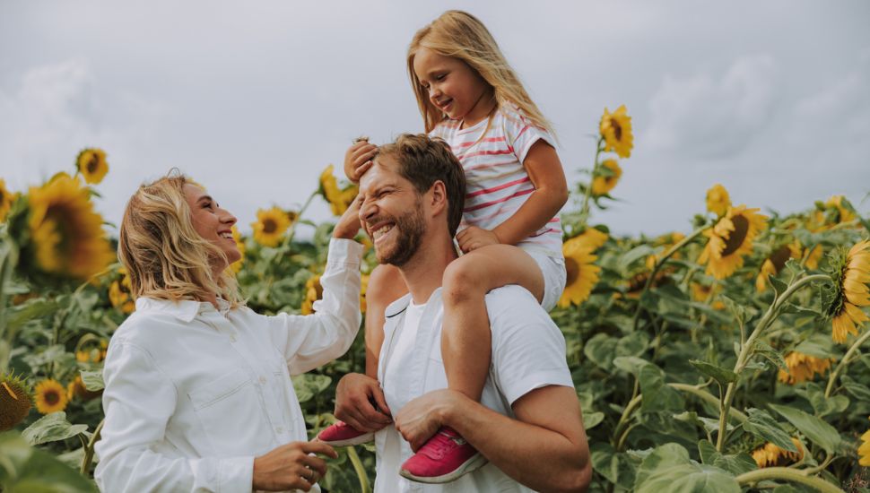 Family of three smiling in a sunflower field.