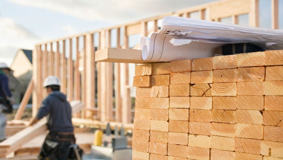 Pile of lumber and man working at a home construction site.