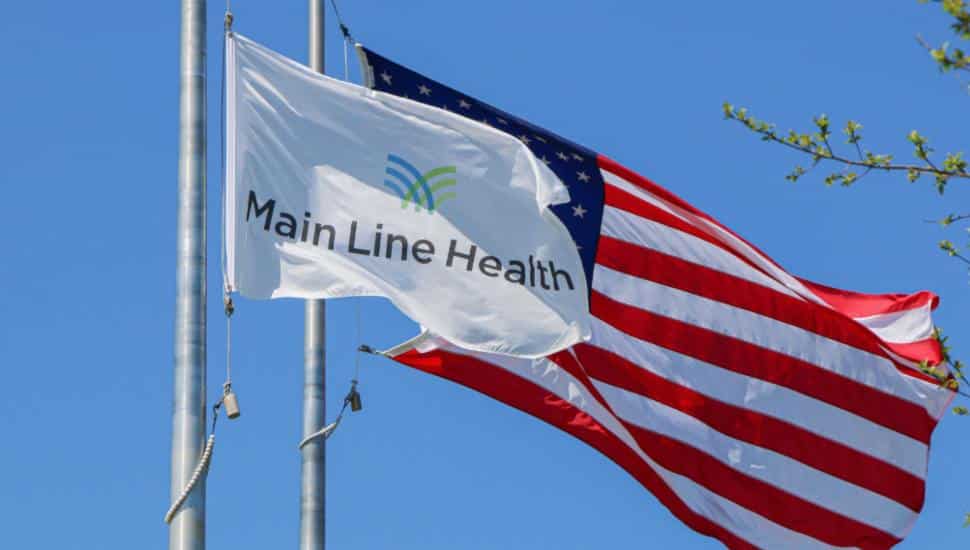 A Main Line Health flag waves in front of the US flag.