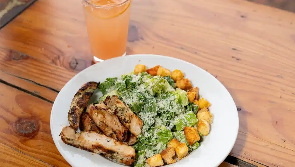 A caesar salad with grilled chicken and croutons, and a drink.