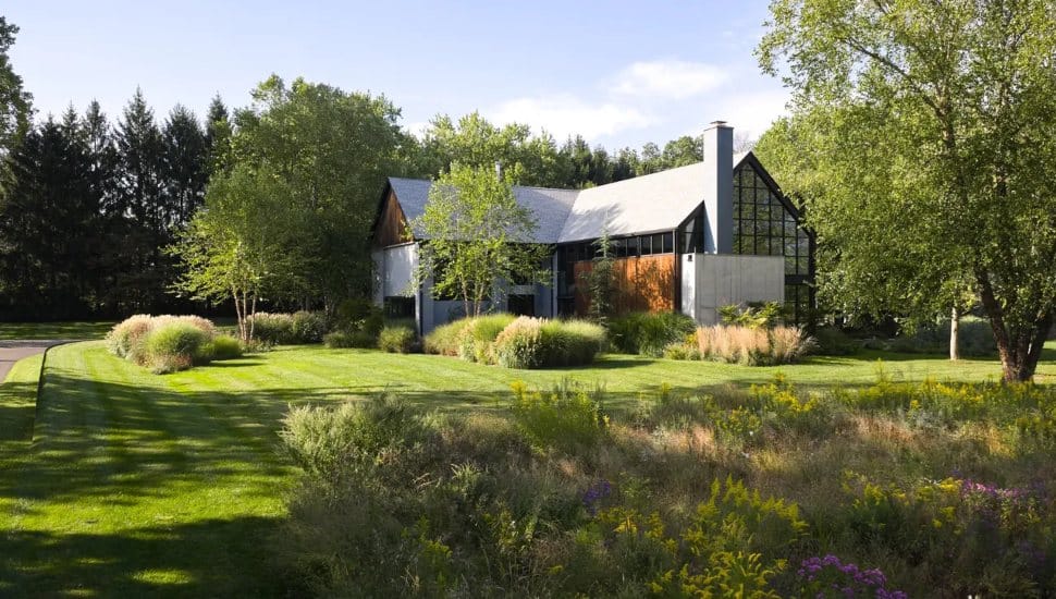 Large estate surrounded by trees and greenery with large windows.