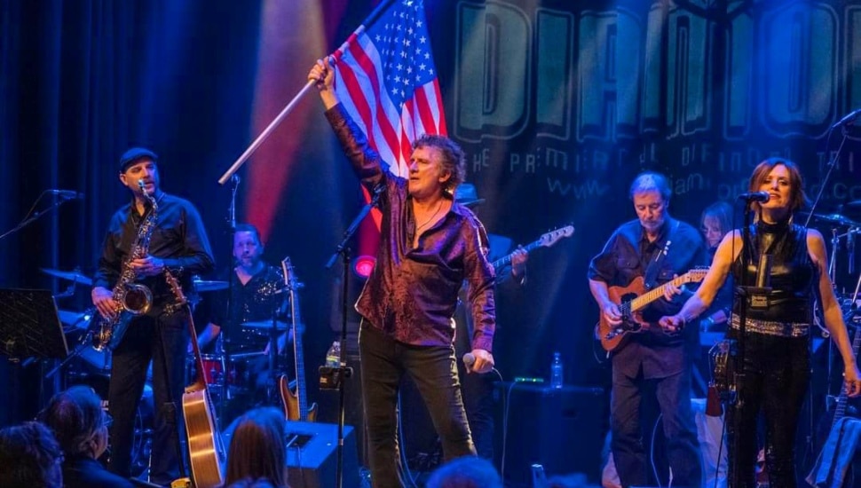Man performing on a stage with American flag in the background.