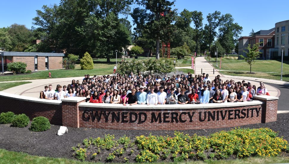 New students pose behind college sign on campus.