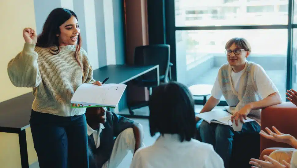 A student confidently presents a project to classmates in a modern classroom environment.