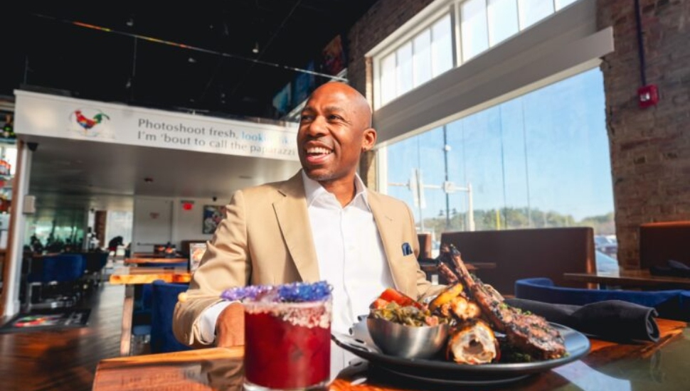 Kevin Kelley smiles while enjoying a plate of food and a drink.