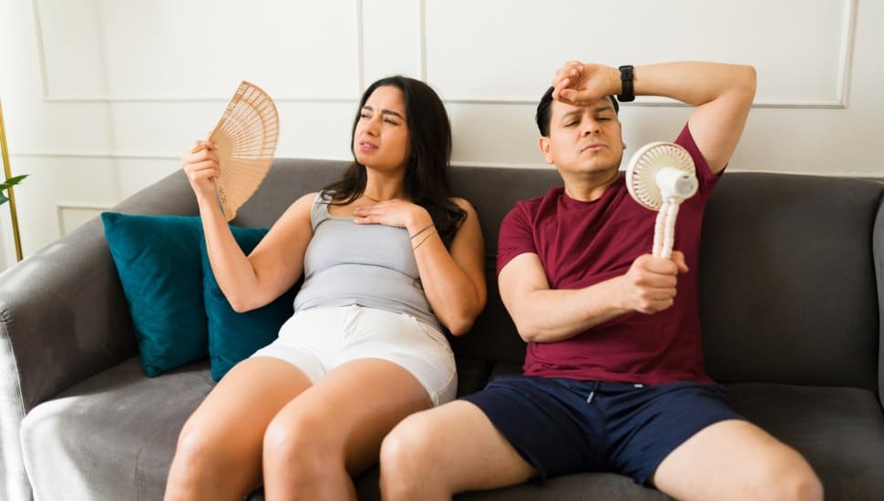 Two people sitting on a couch using fans.