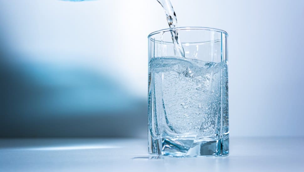 Fresh water being poured into a clear glass against a blue background.