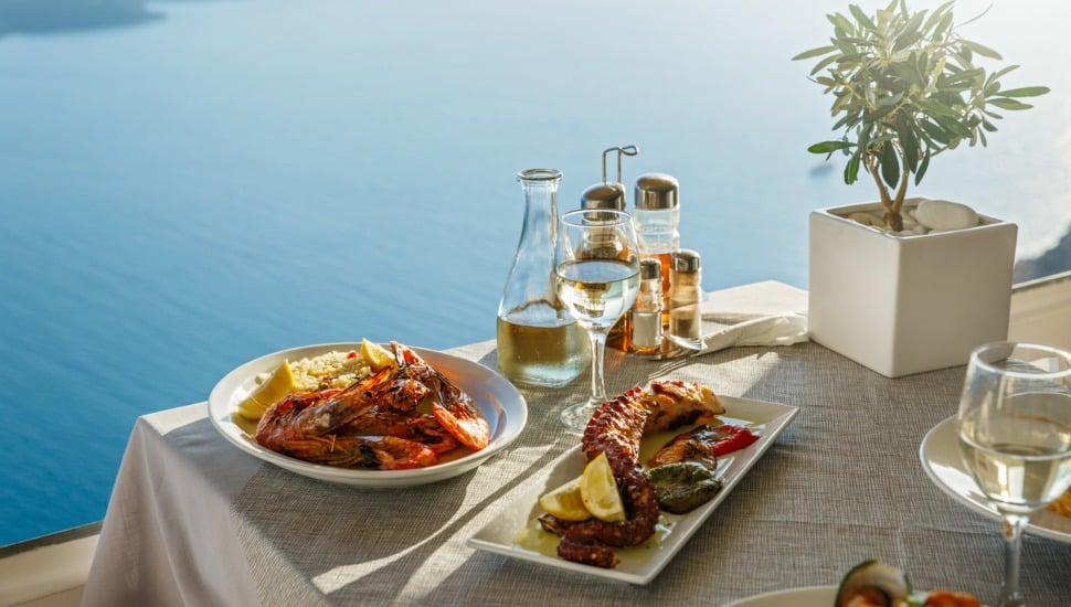 An outdoor setting with seafood entrees and white wine overlooking the ocean.