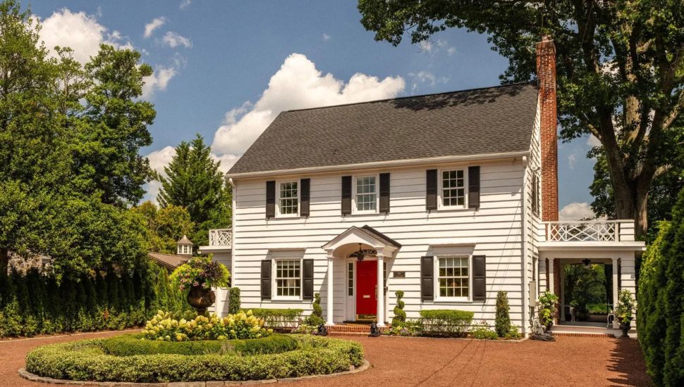 White colonial home with a circular garden surrounded by trees and shrubbery.