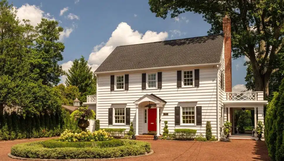 White colonial home with a circular garden surrounded by trees and shrubbery.