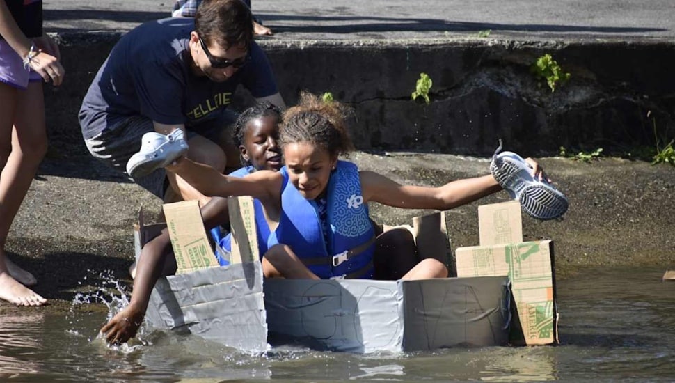 Middle-school students float in a cardboard boat.