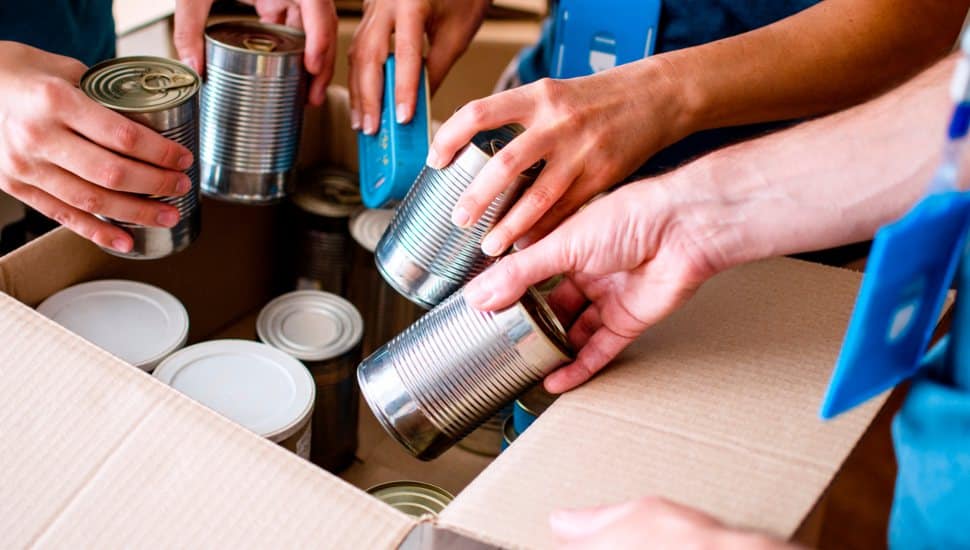 Hands placing donations into cardboard box.
