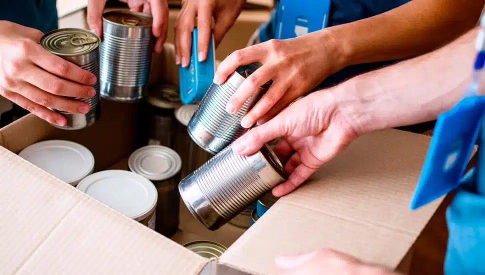 Hands placing donations into cardboard box.