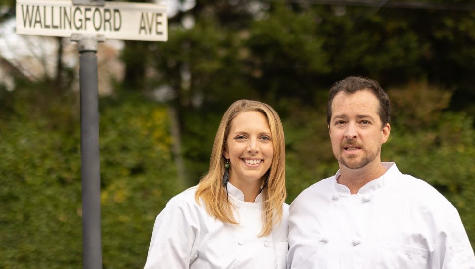 Fond owners in chef outfits standing outside next to Wallingford street sign.