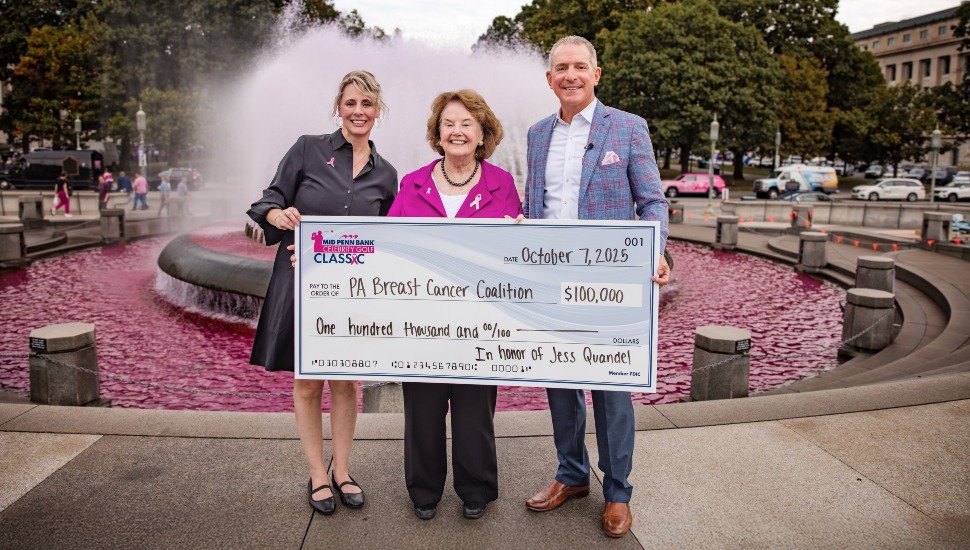 Bank CEO presents check to nonprofit with pink fountain in background.