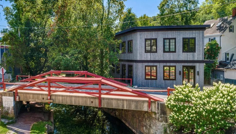 Gray contemporary home with a red footbridge in front of it.