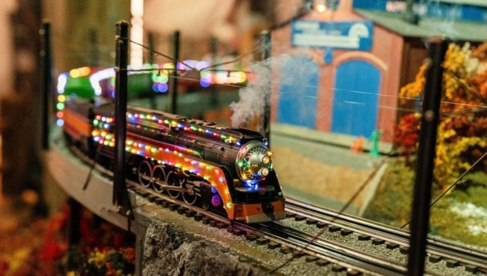 A model train in motion decorated with Christmas lights.