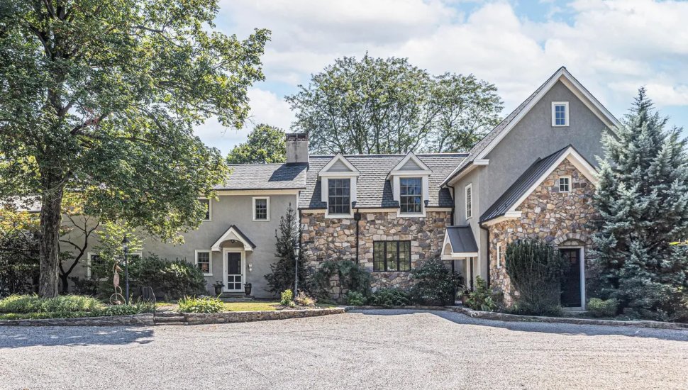 Colonial-style home with stone walls and a tree.