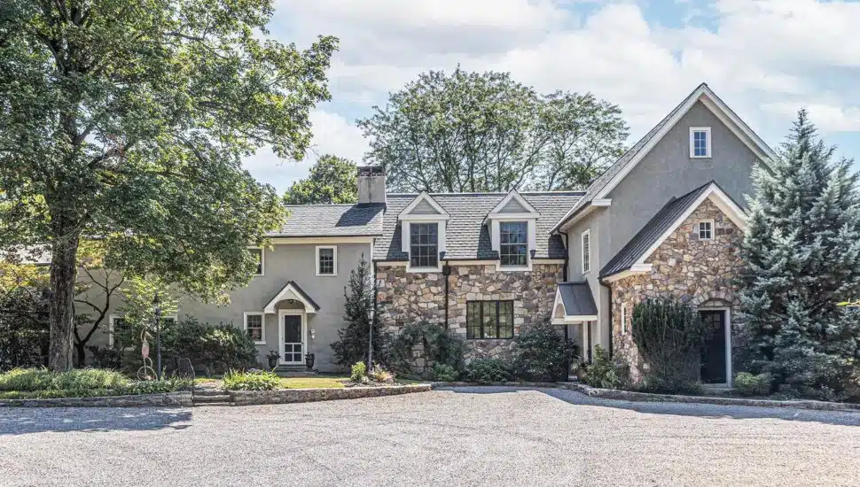 Colonial-style home with stone walls and a tree.