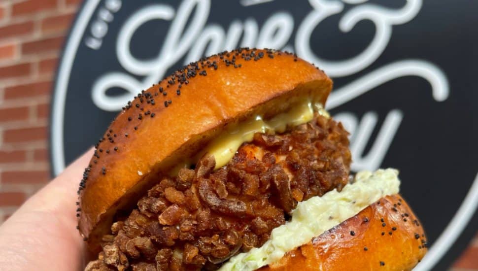 A fried chicken sandwich is held outside of a Love & Honey Fried Chicken restaurant.