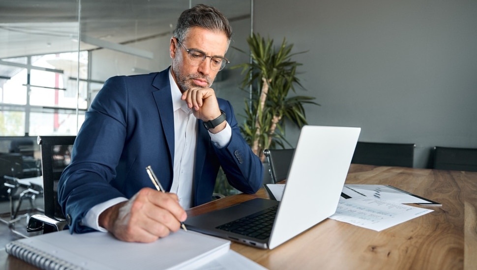 Middle-aged businessman sitting at desk working on laptop writing.