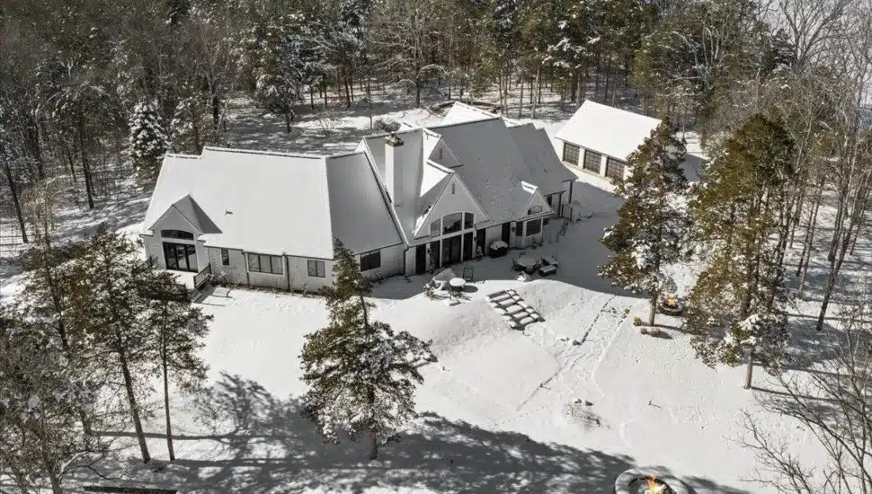 White home covered in snow surrounded by trees.