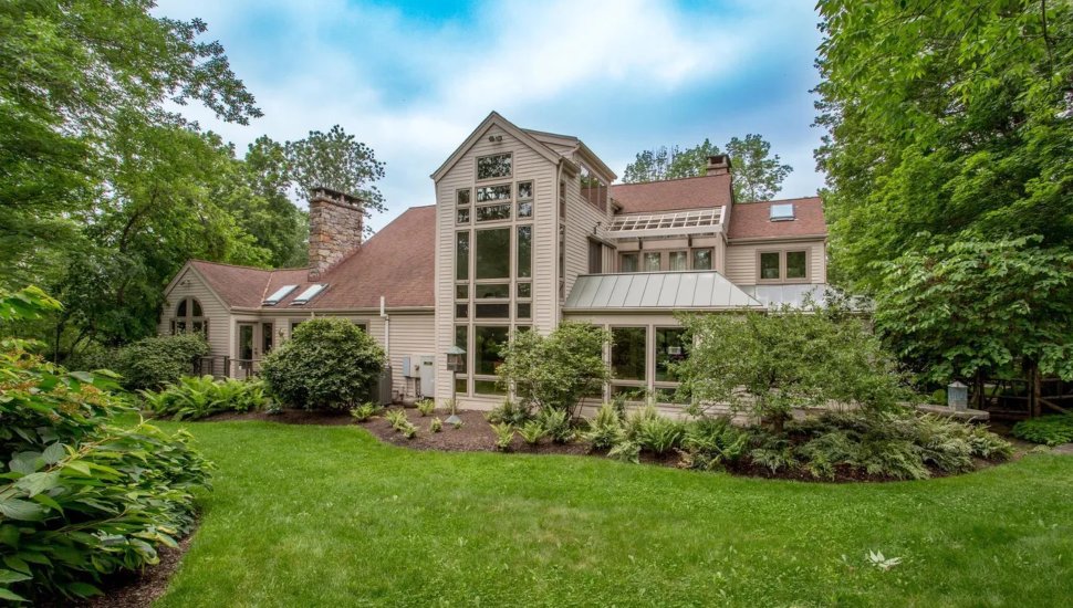 White house with panel siding and large windows surrounded by trees.