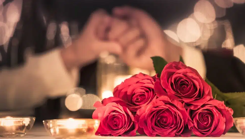 Roses on a table with a couple holding hands in the background.