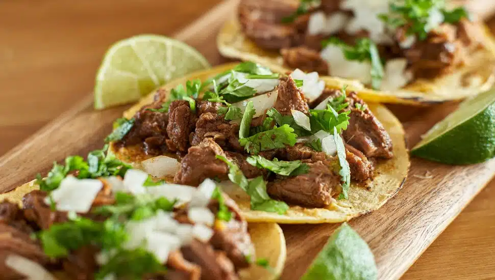 Tacos with lime wedges on a wood board.