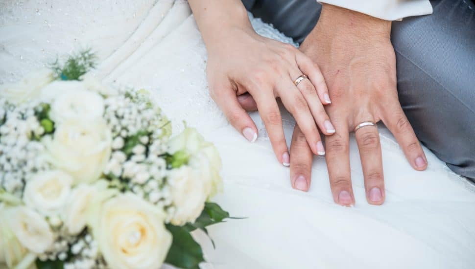 hands of a just married couple with the wedding rings and bouquet.