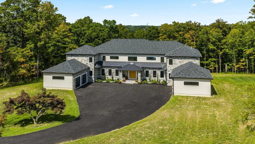 Large stone home with dark gray roofing and an expansive driveway.